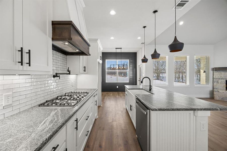 Kitchen with white cabinetry, dark wood finished floors, dark stone countertops, a center island with sink, and hanging light fixtures