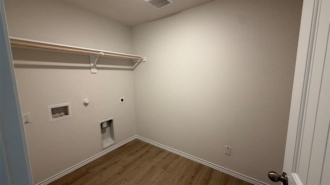 Dedicated utility room featuring wood-finish flooring, light neutral walls, a built-in hanging rod, and appliance hookups