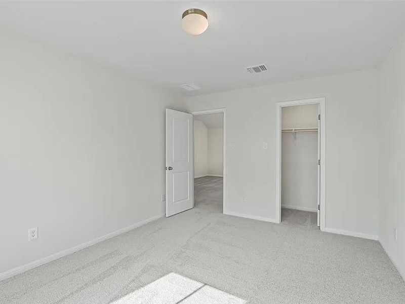 A well-lit bedroom featuring soft carpeting and a spacious closet, offering comfort and practical storage.
