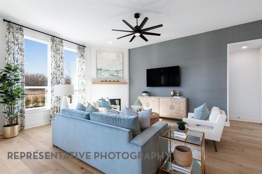 Living room with light wood finished floors, a ceiling fan, a glass covered fireplace, an accent wall, and wallpapered walls