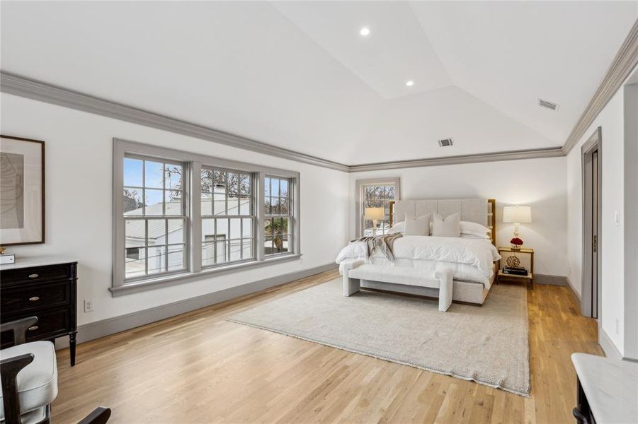 Bedroom with ornamental molding, light wood-style floors, visible vents, and vaulted ceiling