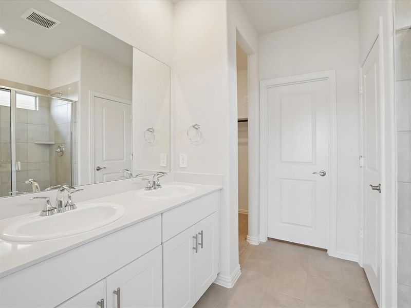 Bathroom featuring double vanity, a shower stall, and light tile patterned floors