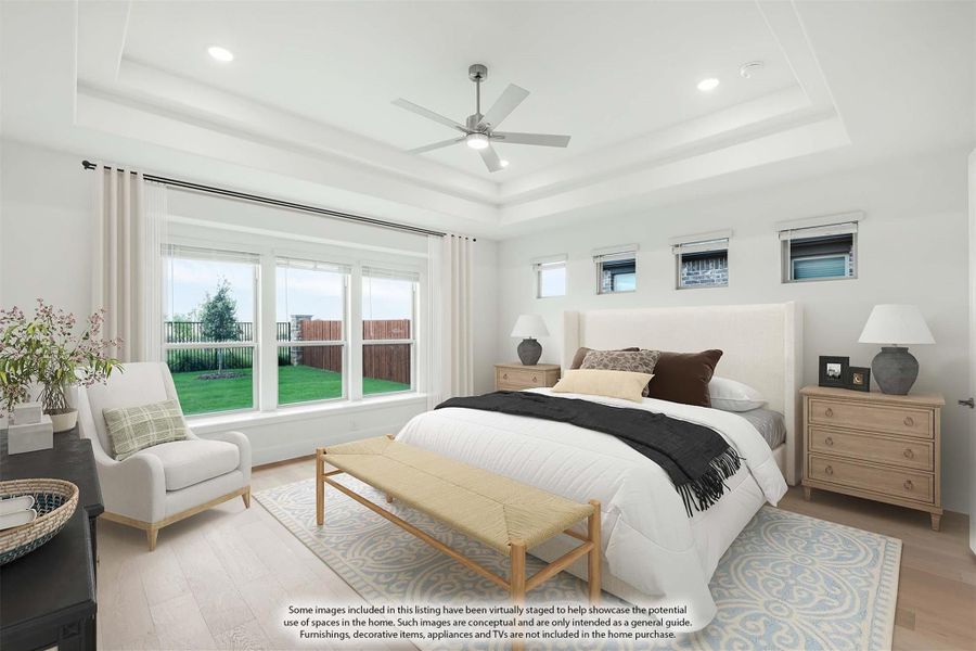 Spacious master bedroom with tray ceiling, ceiling fan, large windows, and light hardwood floors