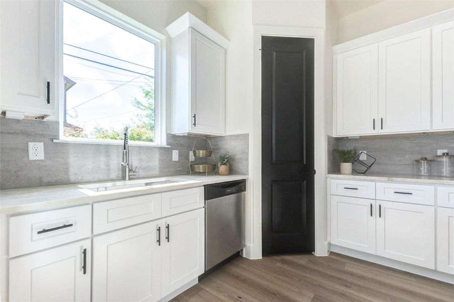 The functional kitchen design includes a deep basin sink, integrated dishwasher, and a contrasting black pantry door.