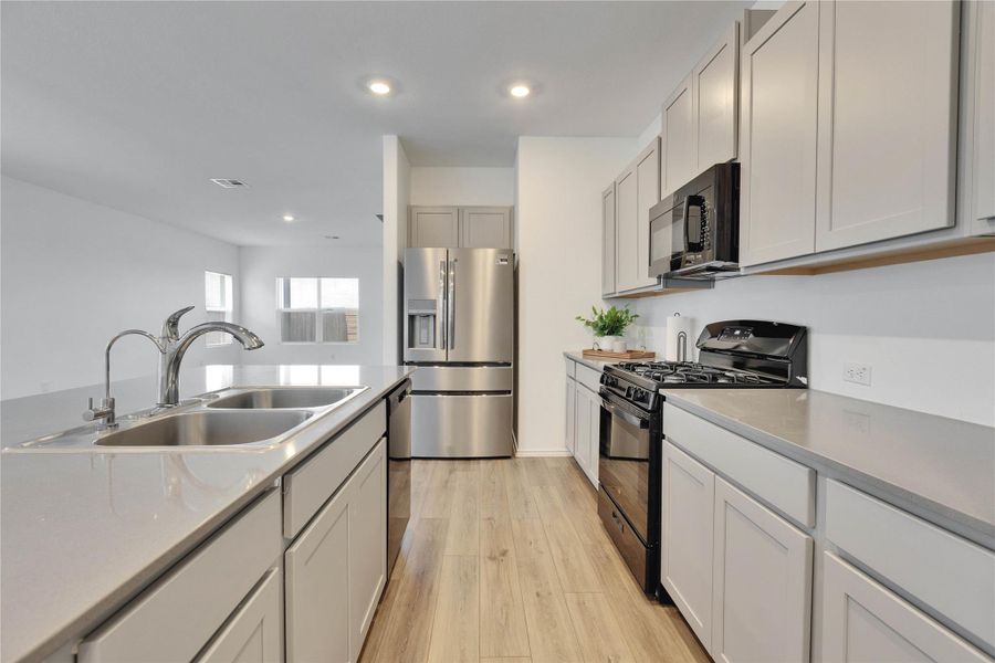 Kitchen with black and stainless steel appliances, light wood-vinyl flooring, recessed lighting, and grey quartz countertops. Kitchen with black and stainless steel appliances, light wood-vinyl flooring, recessed lighting, and grey quartz countertops.