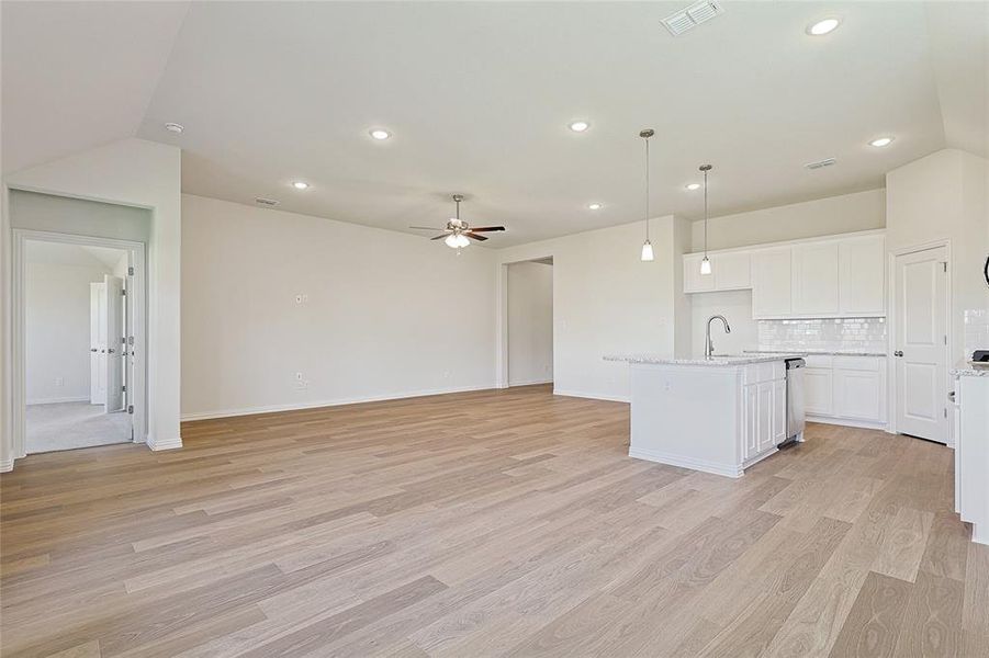 Kitchen with white cabinets, a center island with sink, vaulted ceiling, pendant lighting, and light hardwood / wood-style floors