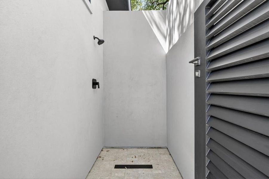 Outdoor shower featuring matte black fixtures, light-toned tile flooring with a linear drain, and privacy walls Outdoor shower featuring matte black fixtures, light-toned tile flooring with a linear drain, and privacy walls