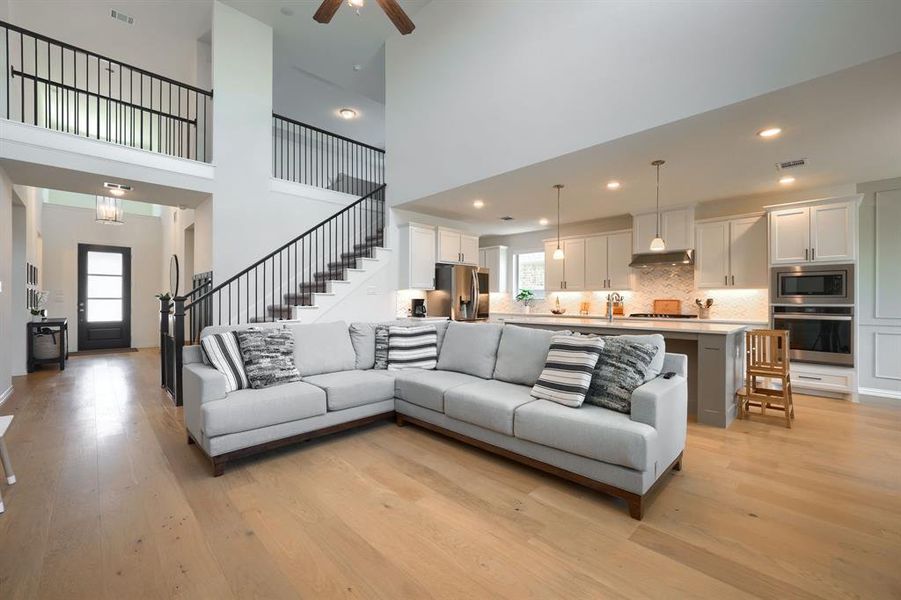 Living room with a towering ceiling, ceiling fan with notable chandelier, and light hardwood / wood-style flooring