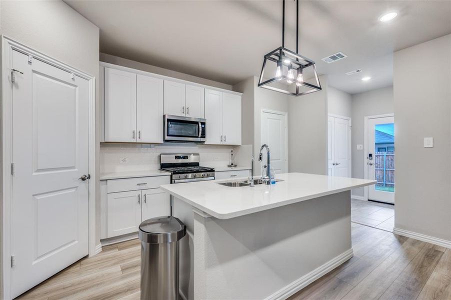 Kitchen with stainless steel appliances, tasteful backsplash, white cabinetry, a center island with sink, and hanging light fixtures