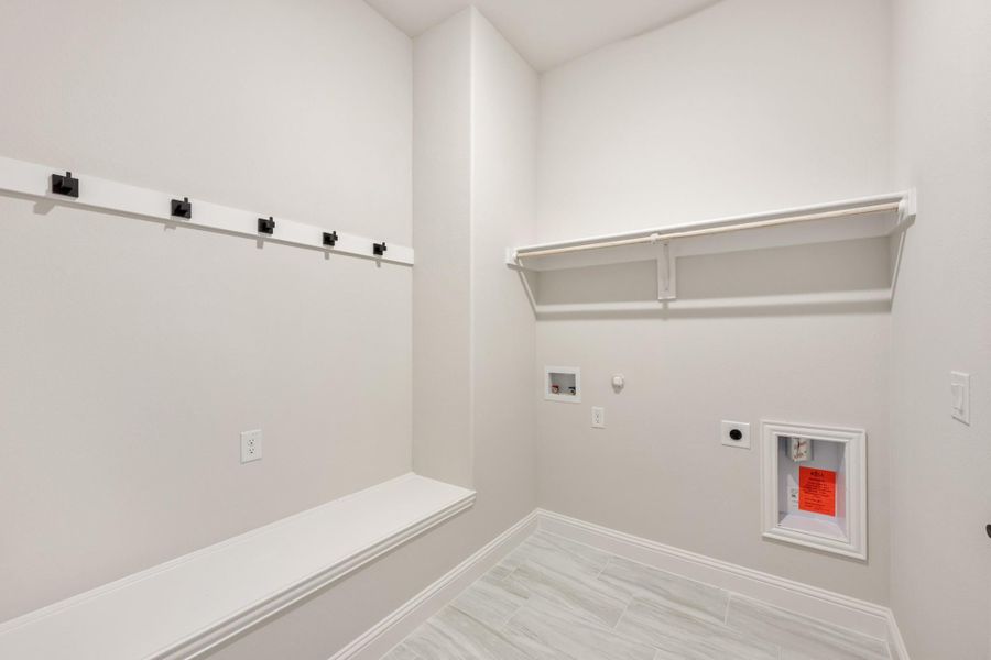 Mudroom and laundry room with black wall hooks, built-in bench, white shelf, and washer hookups on tile floor Mudroom and laundry room with black wall hooks, built-in bench, white shelf, and washer hookups on tile floor