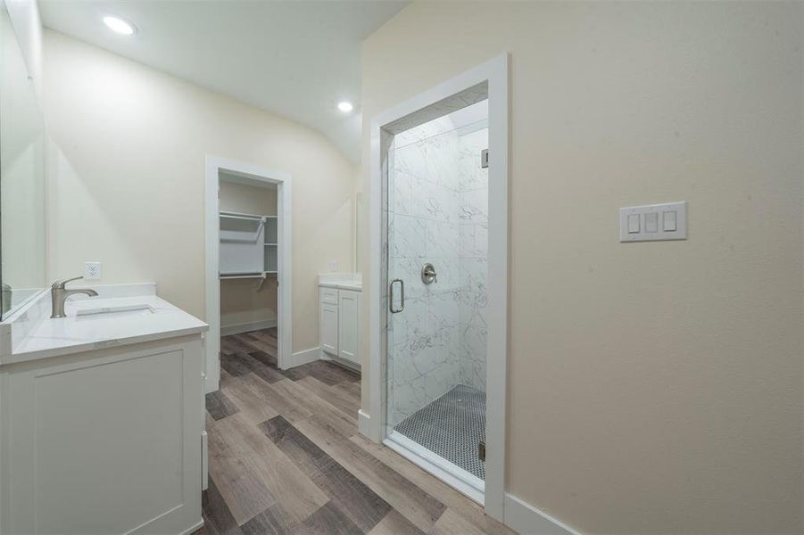 Full bathroom with wood finished floors, vanity, baseboards, a spacious closet, and a marble finish shower