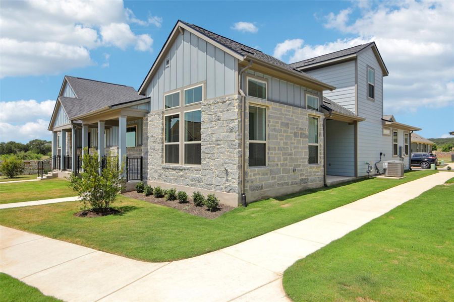 View of side of home with board and batten siding, a yard, stone siding, a porch, and roof with shingles