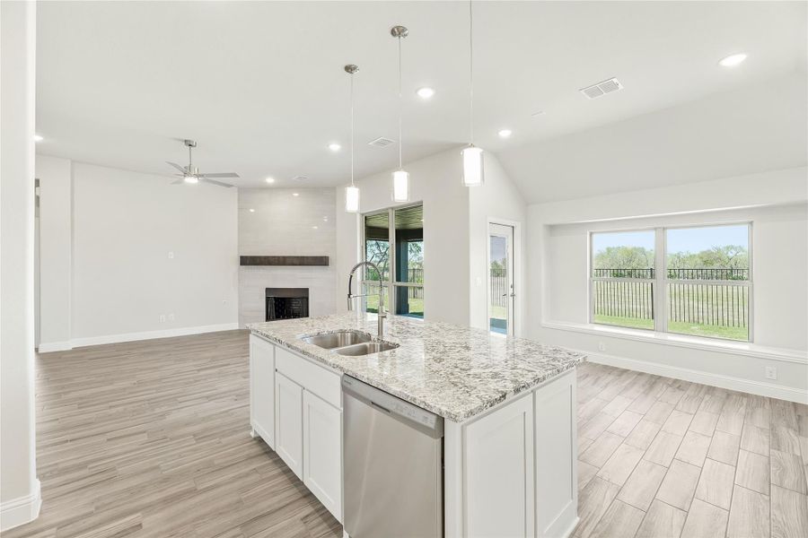 Open kitchen with granite island, white cabinets, and pendant lights, open to living room with fireplace