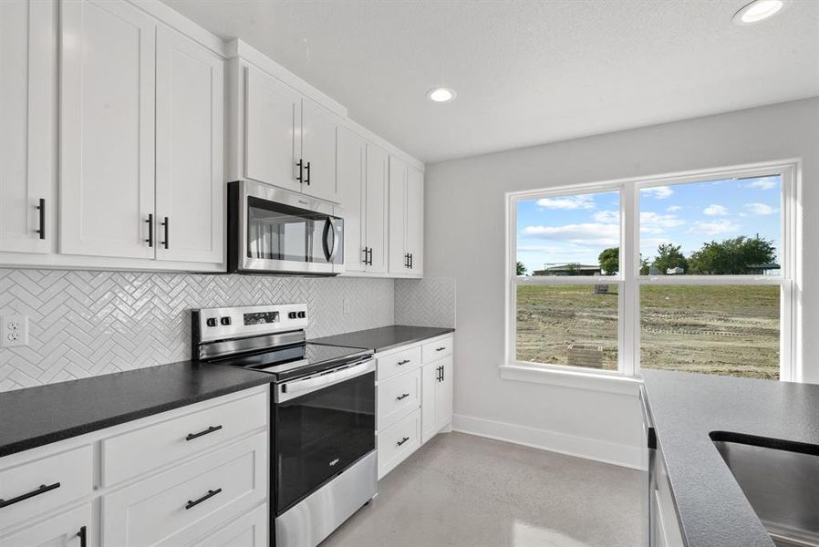 Kitchen featuring appliances with stainless steel finishes, white cabinetry, and tasteful backsplash