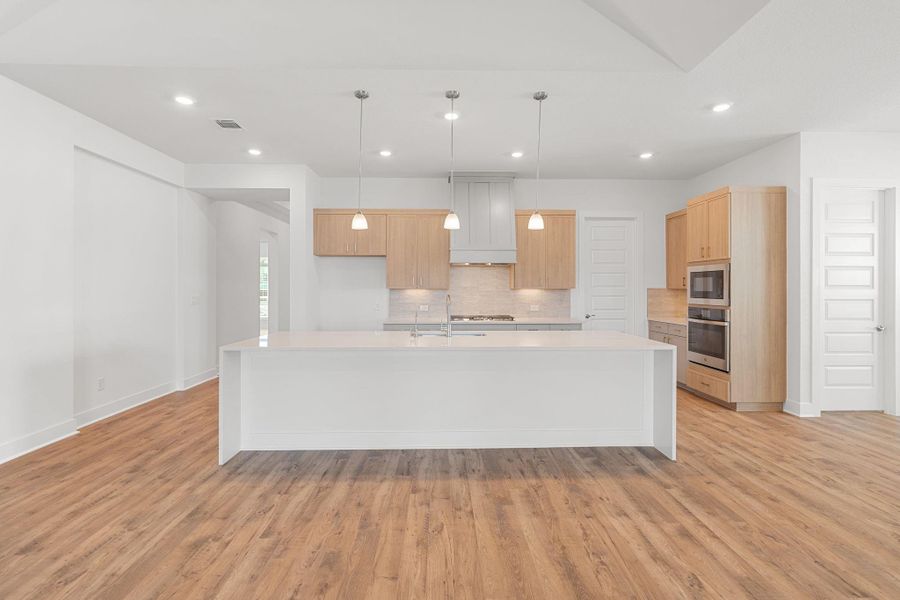 An open-concept culinary space presents a spacious island, built-in appliances, and warm wood flooring.