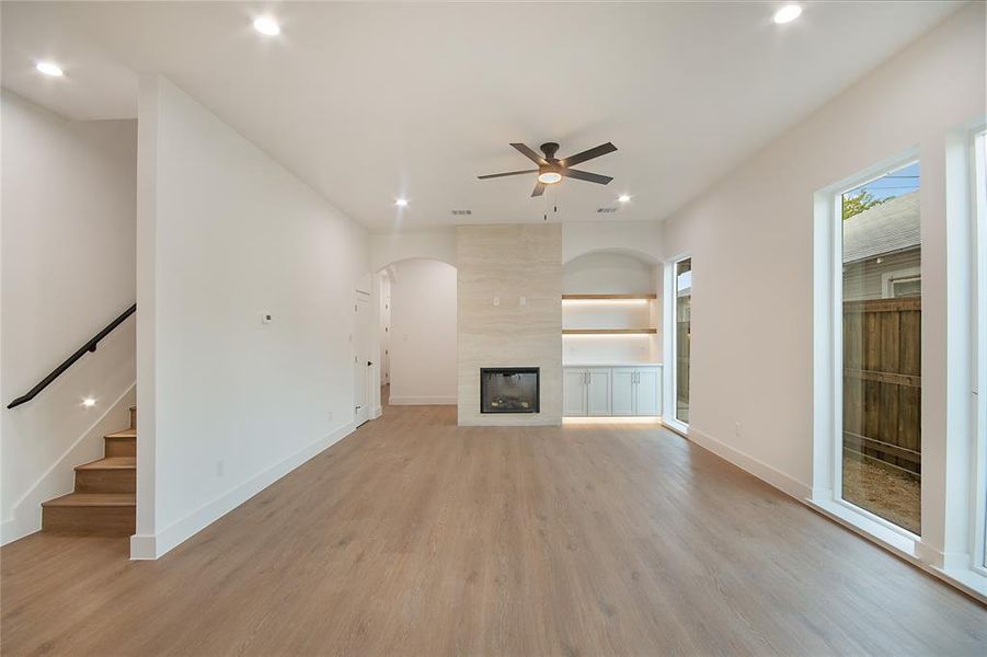 Unfurnished living room featuring light wood-style flooring, a tile fireplace, recessed lighting, stairs, and a ceiling fan