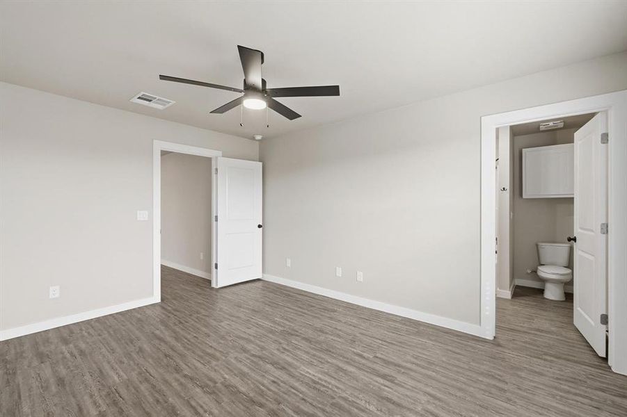 Unfurnished bedroom with ceiling fan, dark wood-style floors, and ensuite bath
