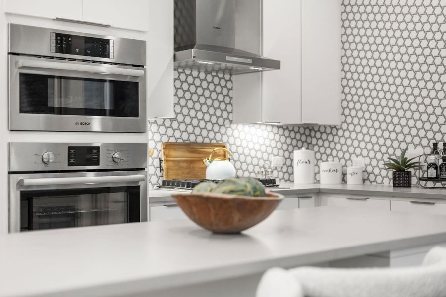 Kitchen with stainless steel appliances, light countertops, white cabinetry, modern cabinets, and wall chimney exhaust hood