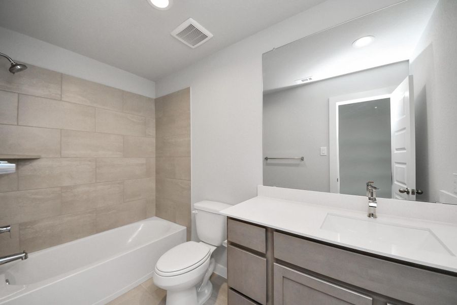 Secondary bath features tile flooring, bath/shower combo with tile surround, light stained wood cabinets, beautiful light countertop.