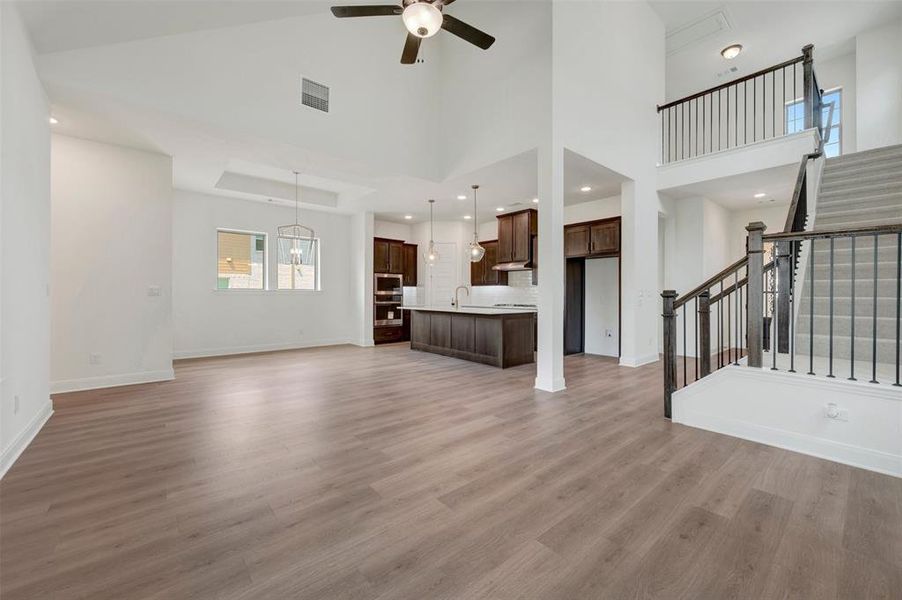 Spacious open-concept interior featuring light wood-finish flooring, vaulted ceilings, and a modern kitchen with dark cabinetry