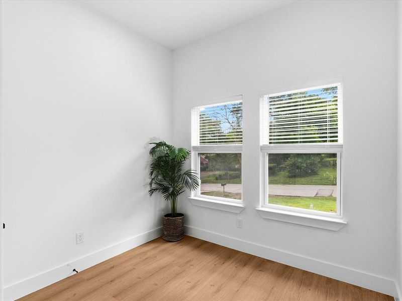 Bright room featuring wood-finish flooring, white baseboards, and two windows with horizontal blinds