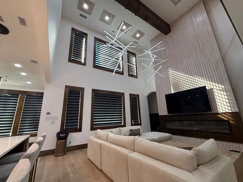 Living room featuring light wood-style flooring, beamed ceiling, a chandelier, recessed lighting, and a towering ceiling