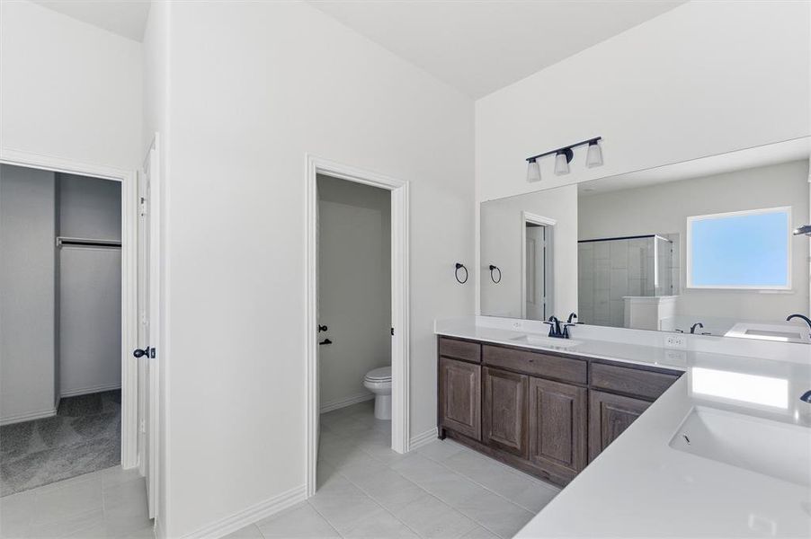 Full bath featuring a stall shower, double vanity, light tile patterned flooring, and a walk in closet