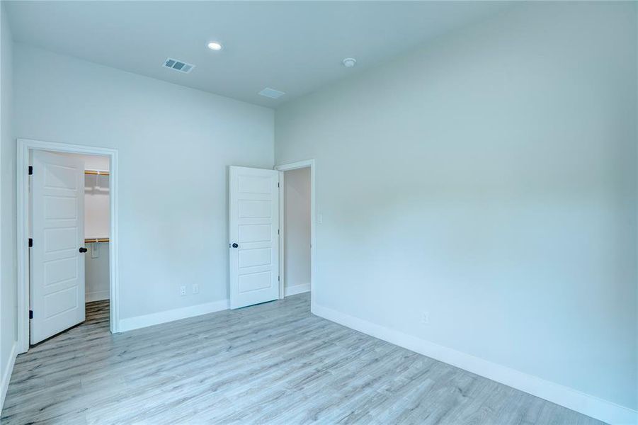 Spacious room featuring light wood-finish flooring, white baseboards, and a recessed ceiling light