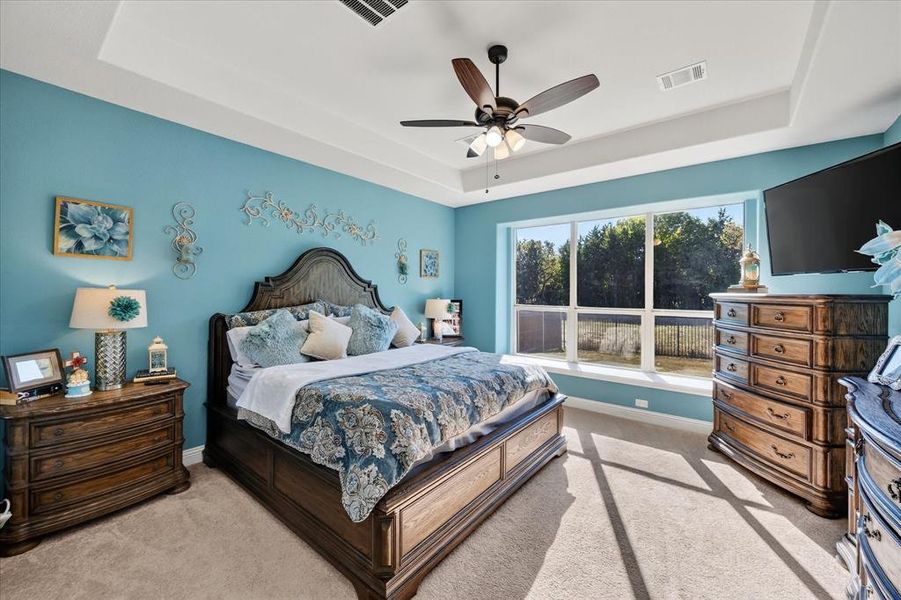 Bedroom featuring a tray ceiling, light colored carpet, and ceiling fan Bedroom featuring a tray ceiling, light colored carpet, and ceiling fan