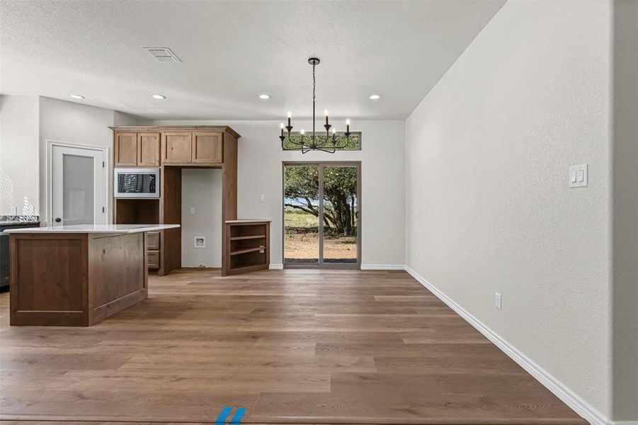 Kitchen with a chandelier, dark wood finished floors, pendant lighting, stainless steel microwave, and light stone countertops