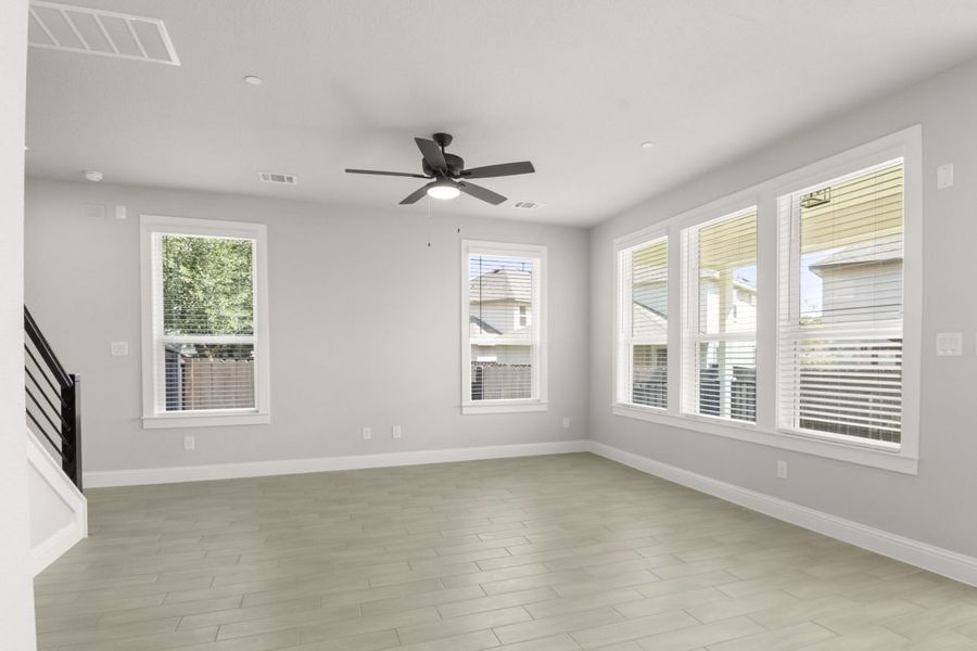 The living room interior with tan vinyl flooring, and white-framed windows, and black ceiling fan.