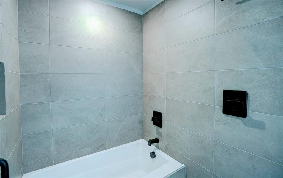 Bathtub with a white basin and a light gray tile surround, featuring matte black fixtures