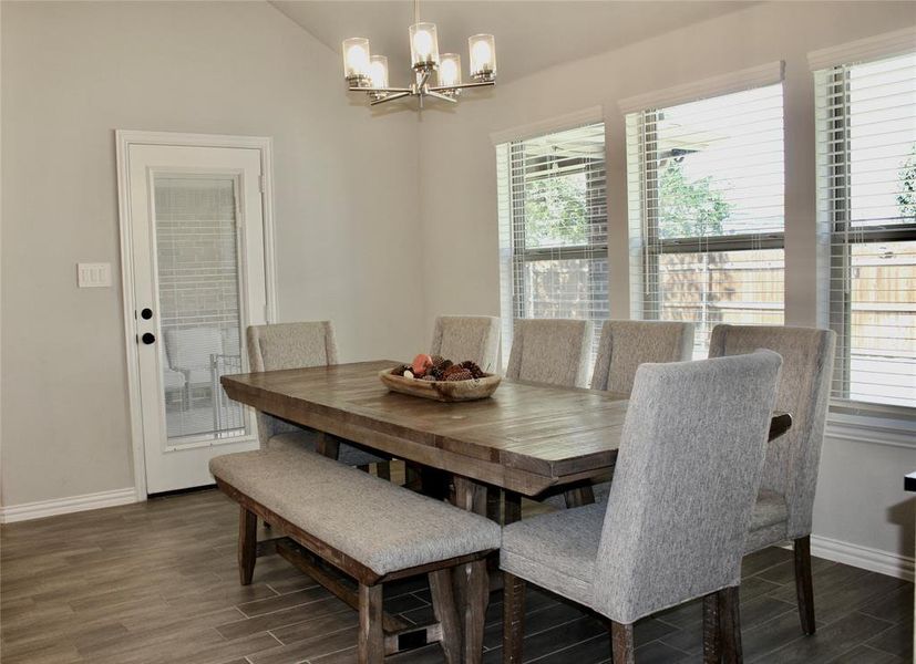 Dining area featuring healthy amount of natural light, wood tiled floors, a chandelier, and vaulted ceiling Dining area featuring healthy amount of natural light, wood tiled floors, a chandelier, and vaulted ceiling