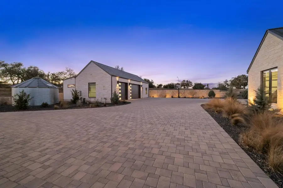 Property exterior at dusk featuring stone siding, an outbuilding, fence, decorative driveway, and a garage Property exterior at dusk featuring stone siding, an outbuilding, fence, decorative driveway, and a garage
