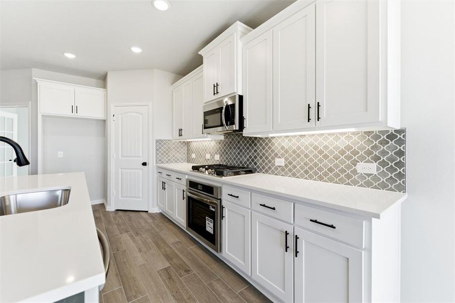 Kitchen with light stone counters, white cabinetry, stainless steel appliances, wood tiled floors, and recessed lighting