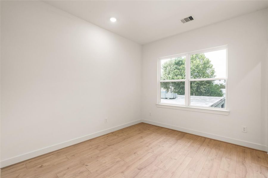 Secondary bedroom — light-filled layout with large picture window, wide-plank wood-look flooring, and crisp modern trim.