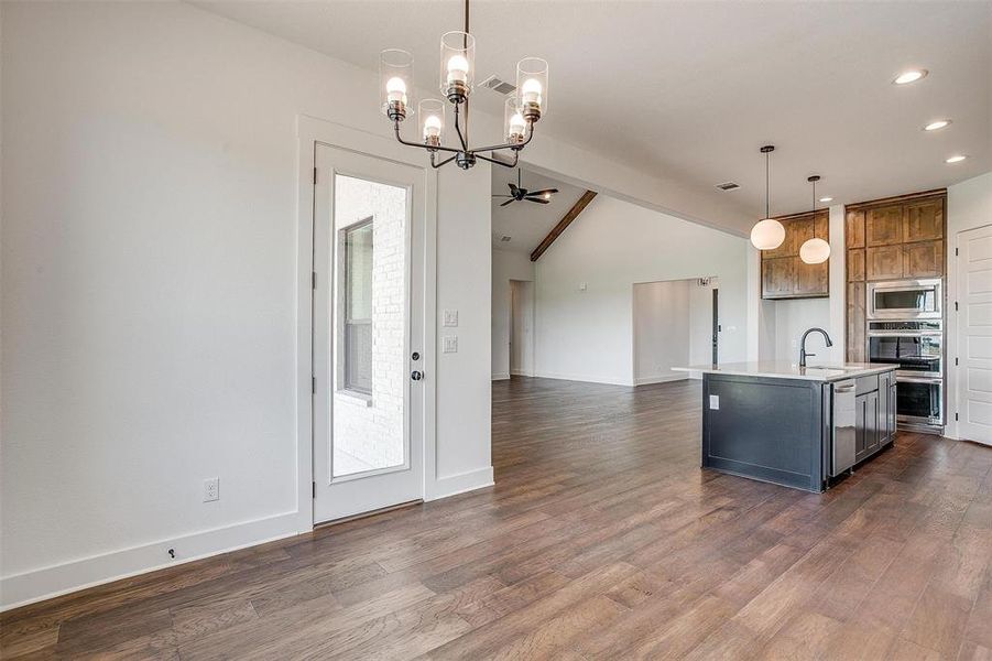 Kitchen featuring lofted ceiling with beams, stainless steel appliances, decorative light fixtures, dark hardwood / wood-style floors, and an island with sink