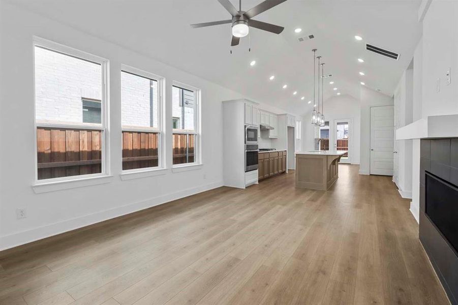 Unfurnished living room with a glass covered fireplace, recessed lighting, light wood-style flooring, high vaulted ceiling, and ceiling fan Unfurnished living room with a glass covered fireplace, recessed lighting, light wood-style flooring, high vaulted ceiling, and ceiling fan
