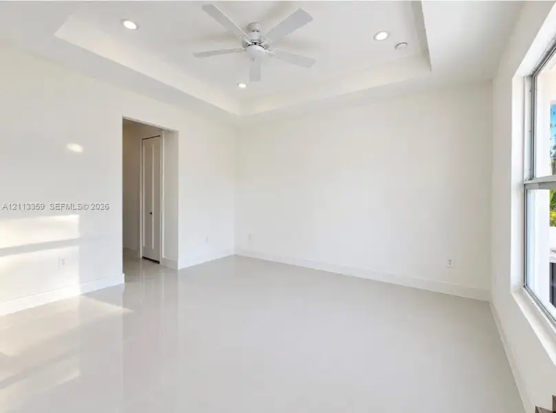 Tray ceiling featuring a central white ceiling fan, recessed lighting, and large-format tile flooring