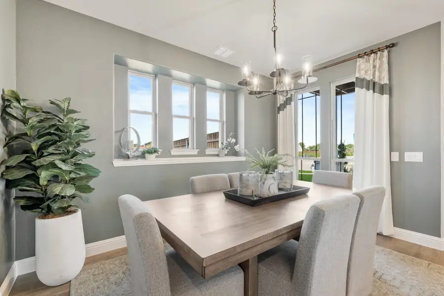 Dining room with wood table, upholstered chairs, chandelier, and large windows with natural light
