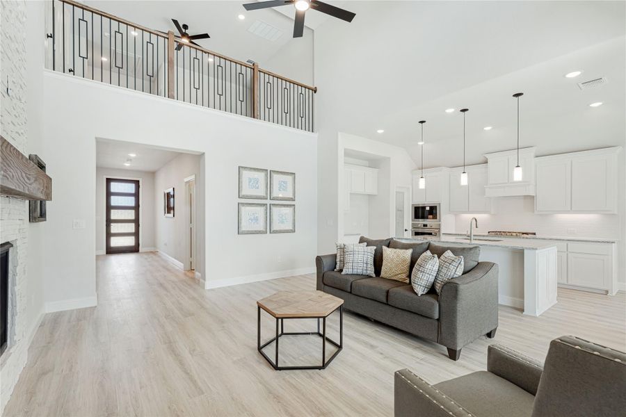 Open-concept living room with two-story ceiling, stone fireplace, and kitchen visible in background