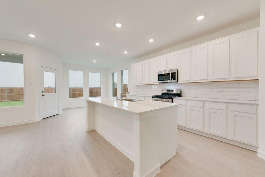 Kitchen with backsplash, an island with sink, white cabinetry, stainless steel appliances, and light wood-type flooring Kitchen with backsplash, an island with sink, white cabinetry, stainless steel appliances, and light wood-type flooring