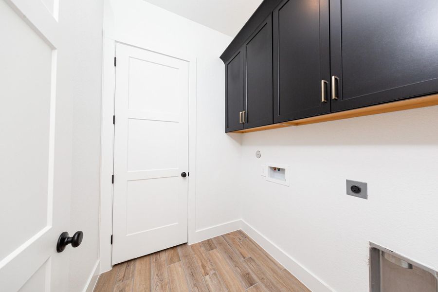 This bright and functional laundry room is conveniently located right off the primary walk-in closet and is ready for your appliances. It features clean white walls, trim, cabinets, and tile flooring.