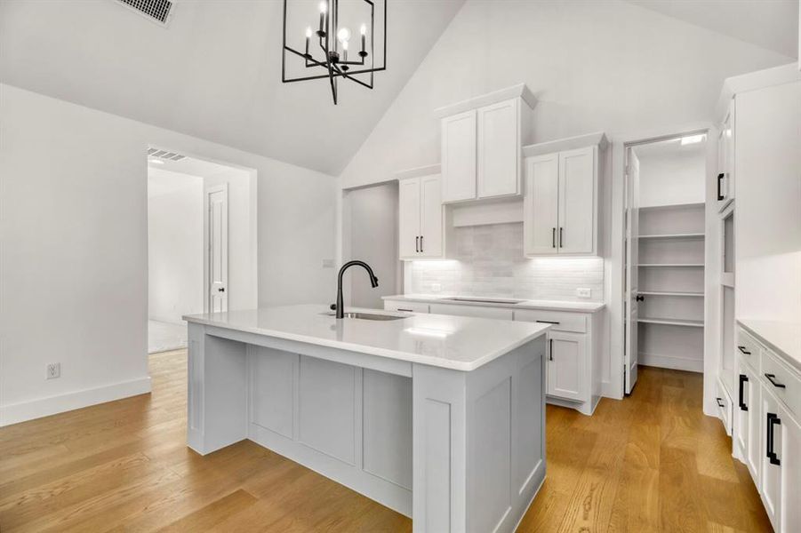Kitchen featuring a center island with sink, vaulted ceiling, white cabinets, and light wood-style floors