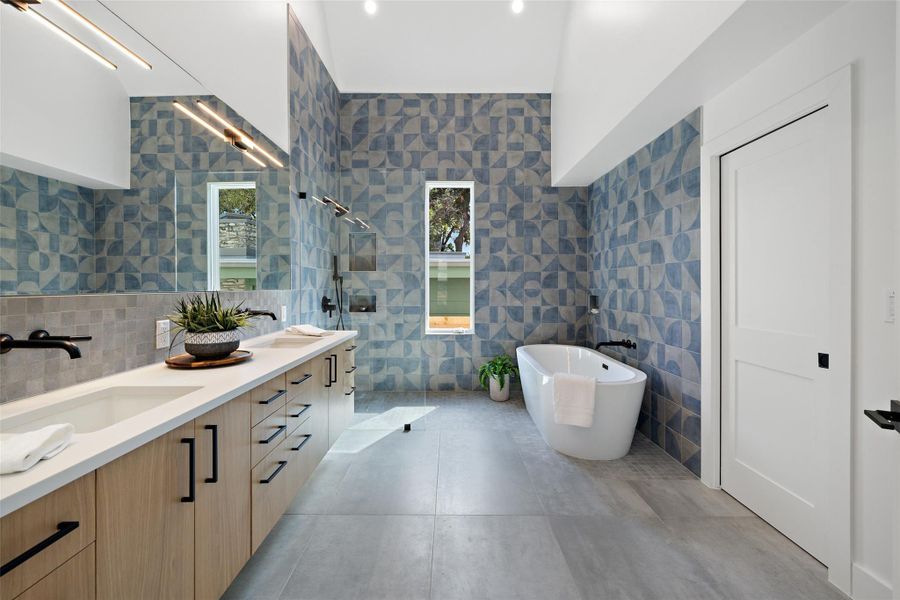 Bathroom featuring walk in shower, double vanity, a freestanding tub, tile walls, and light tile patterned flooring