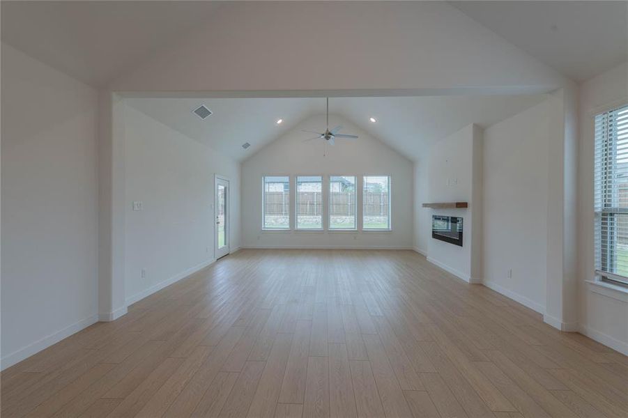 Unfurnished living room with vaulted ceiling, ceiling fan, light wood-style flooring, a glass covered fireplace, and baseboards