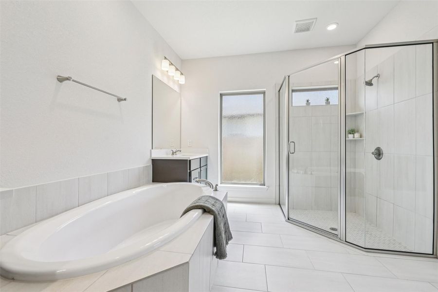 Spacious bathroom featuring a soaking tub, a large glass-enclosed shower, and a vanity with a mirror