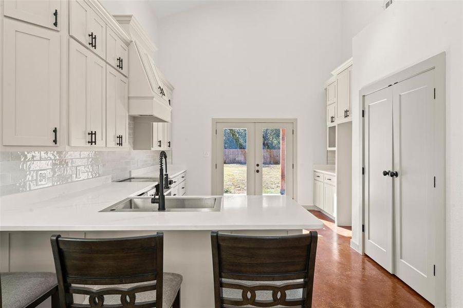 Kitchen with white cabinetry, a breakfast bar, decorative backsplash, a peninsula, and high vaulted ceiling