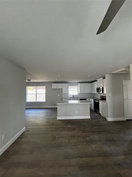 Kitchen with dark wood-type flooring, sink, white cabinets, range, and a center island