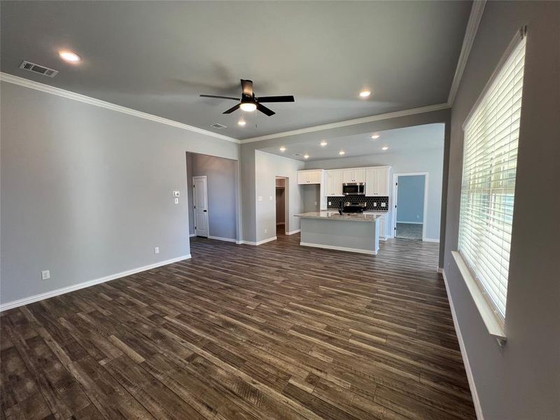 Unfurnished living room featuring ceiling fan, ornamental molding, and dark wood-type flooring